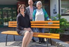 Frau sitzt auf oranger Bank, der Bürgermeister der Gemeinde Kirchbach und eine weitere Frau stehen dahinter. (c) Gemeinde Kirchbach